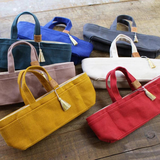 A collection of colorful handbags and purses, including blue, pink, white, and red, are arranged on a wooden surface.