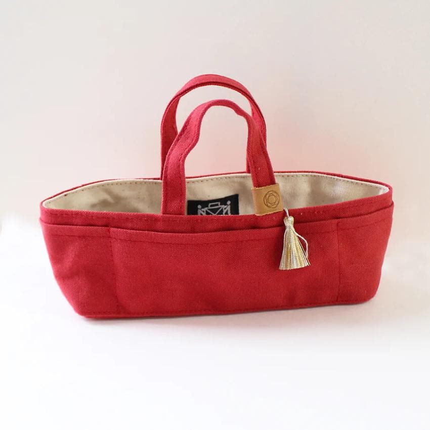 A red tote bag with a tassel hanging from the handle, sitting on a white surface.