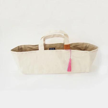 A beige canvas tote bag with a pink tassel hanging from the handle.