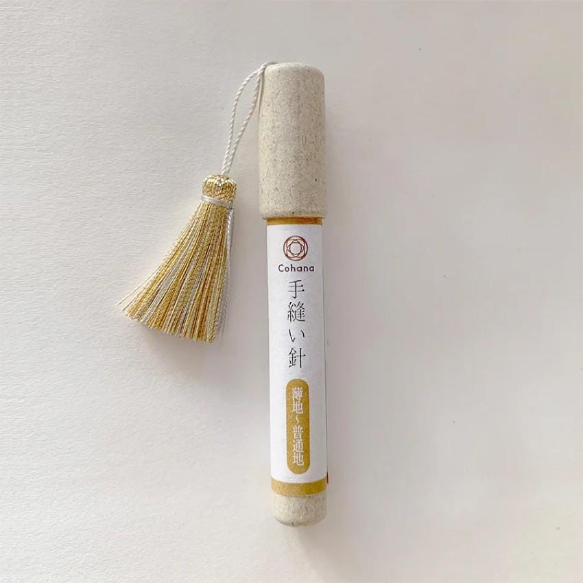 A white cylindrical object with a gold tassel attached, featuring Japanese text and a logo.