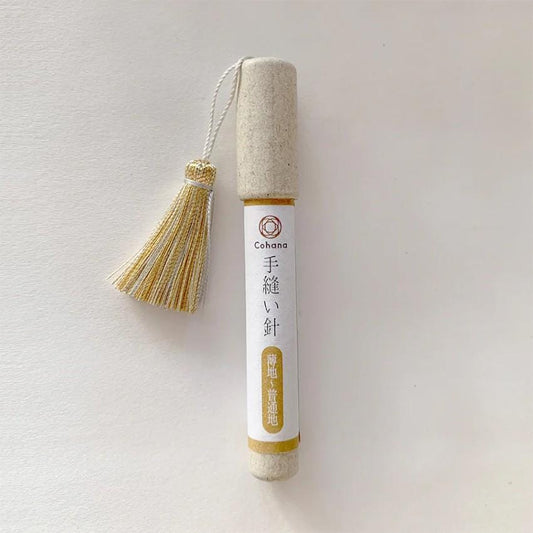 A white cylindrical object with a gold tassel attached, featuring Japanese text and a logo.