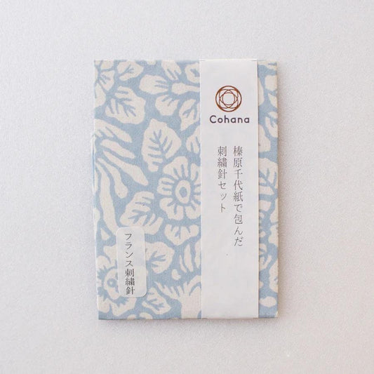 A light blue and white floral patterned paper with Japanese text and a circular logo.