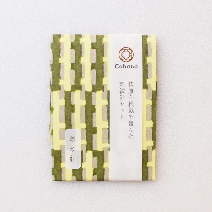 a book cover with a repeating pattern of green and yellow blocks, and a white label with Japanese text.