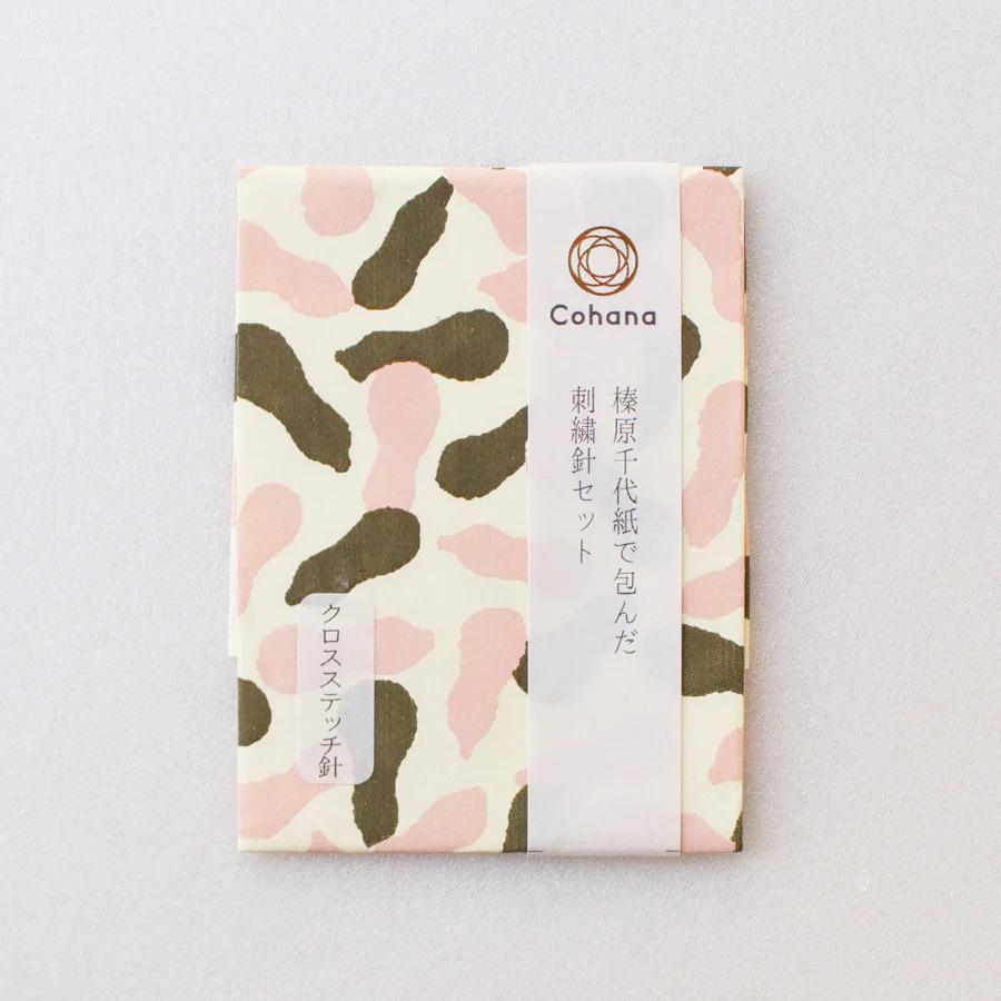 A square-shaped paper with a camouflage pattern in shades of pink and green, featuring Japanese text and a logo.
