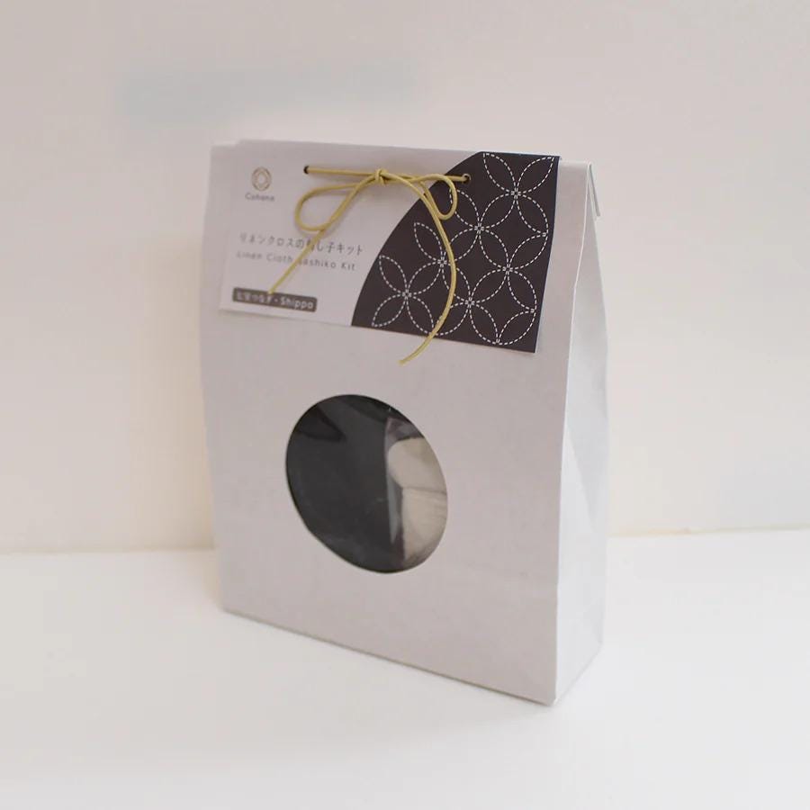 A white paper bag with a black and white patterned design, featuring a circular cutout on the front.