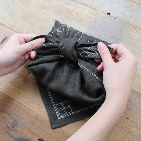 A pair of hands is carefully folding a black cloth napkin with a scalloped edge, creating a neat and tidy appearance.