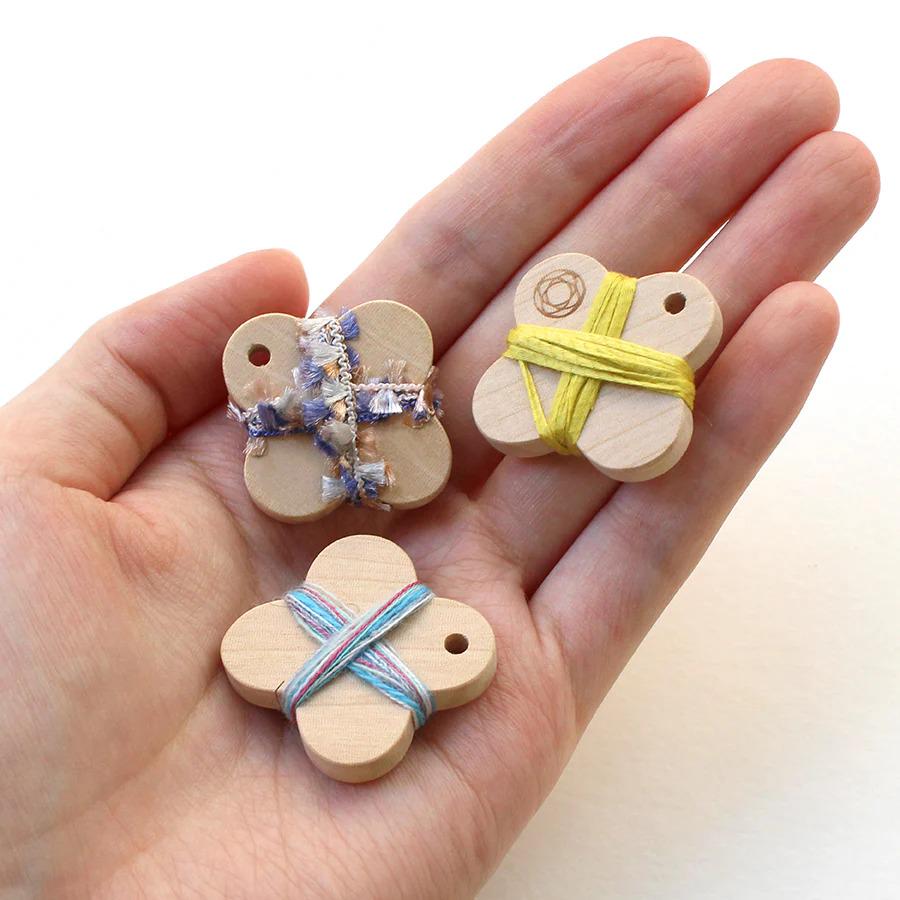A hand holding three small wooden objects, each tied with a string.