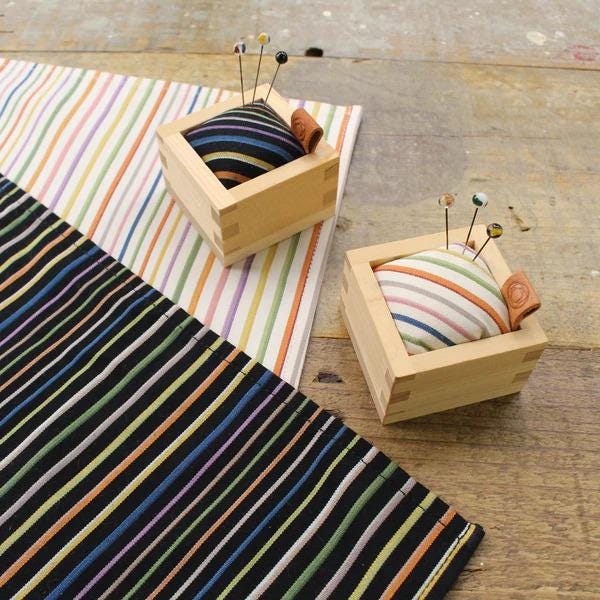 two wooden boxes with colorful pin cushions, placed on a wooden surface.
