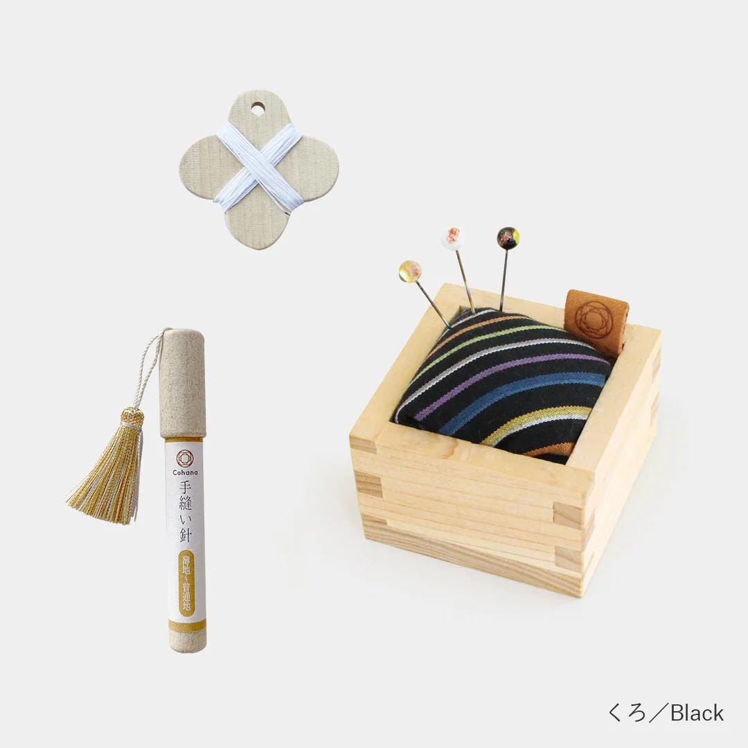 a wooden box with a black and white striped cushion, a wooden pin cushion, and a wooden pin holder.