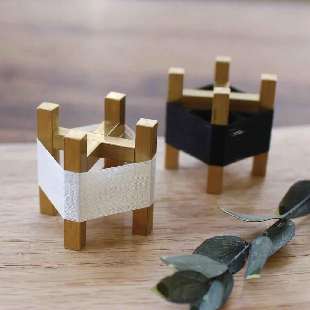 two small wooden stands, one with a white cloth and the other with a black cloth, placed on a wooden surface alongside some green leaves.
