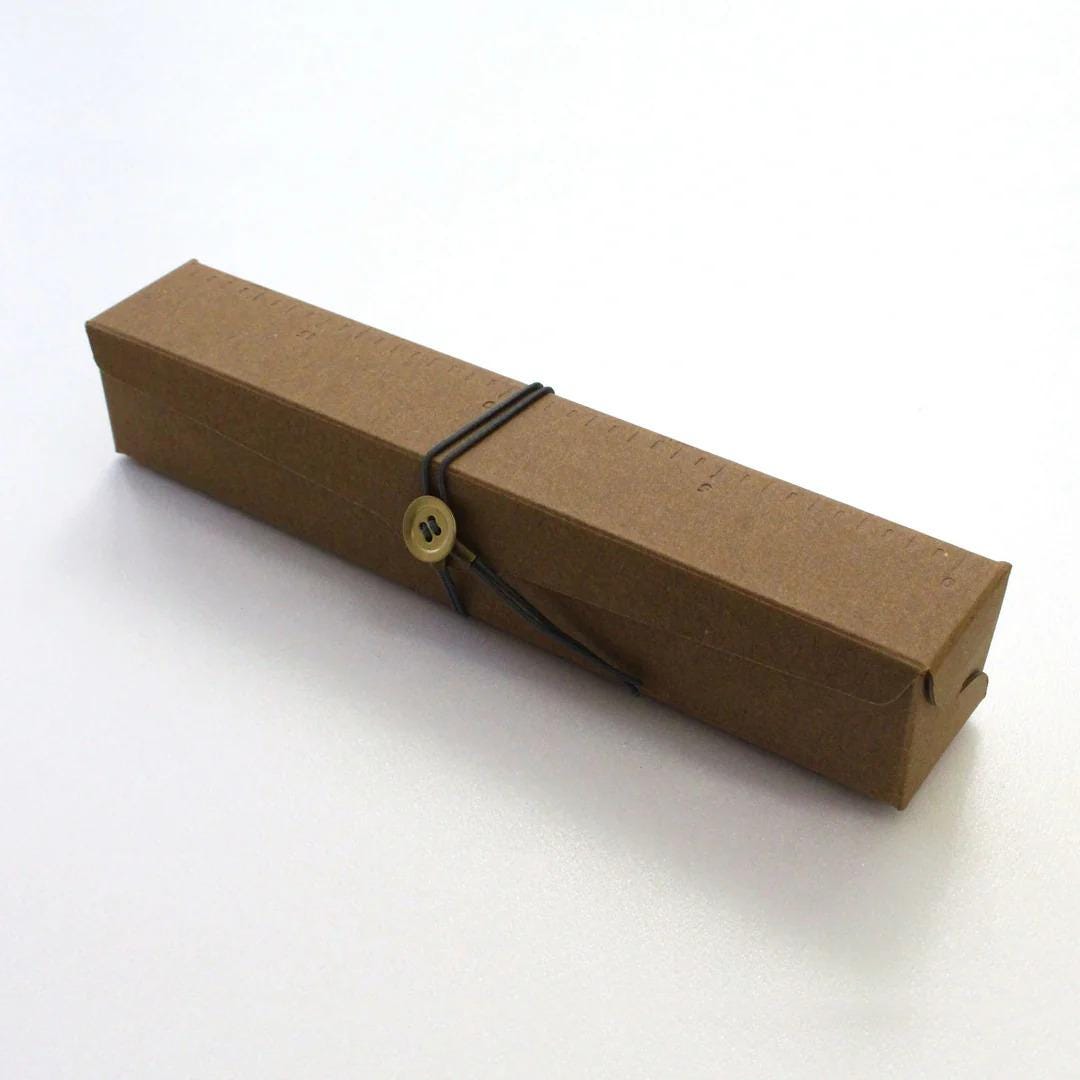 A brown cardboard box with a black rubber band and a gold button on it, sitting on a white surface.