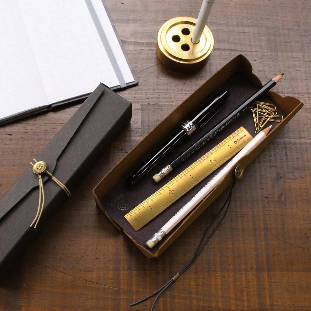 a collection of office supplies, including a pen, pencils, and a ruler, arranged on a wooden surface.
