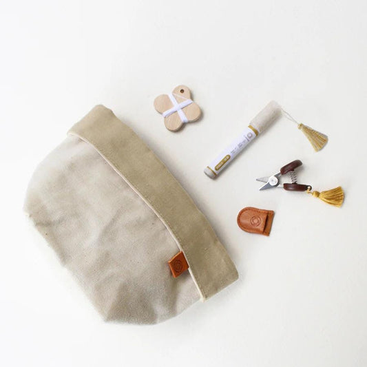 A beige canvas bag with a tassel, a small wooden object, a white marker, and a pair of scissors are arranged on a white background.