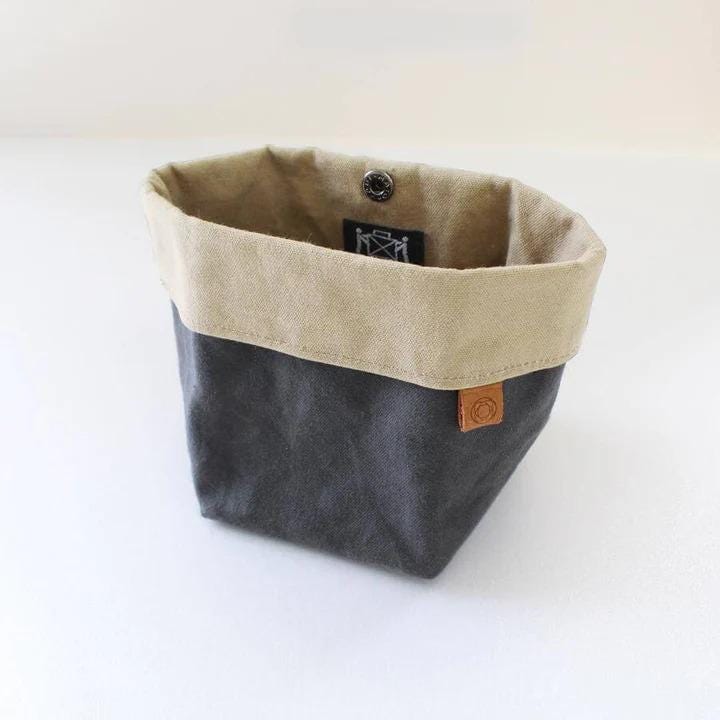 A gray and beige canvas storage bin with a leather tag attached, sitting on a white surface.