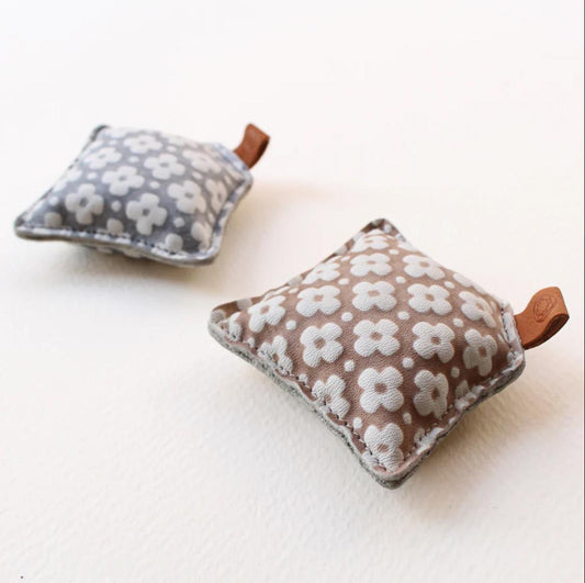 two small, square-shaped fabric pouches with a floral pattern, each attached to a brown leather tag.
