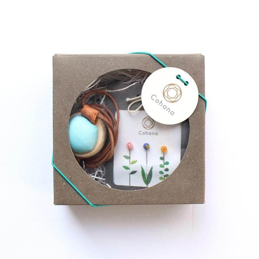A gift box containing a necklace, a small plant, and a tag with the brand name "Cohana".