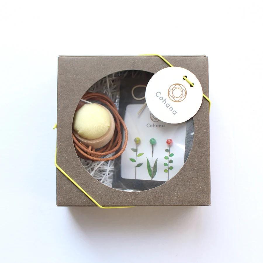 A brown cardboard box containing a small white ball, a brown string, and a small white card with a plant design.