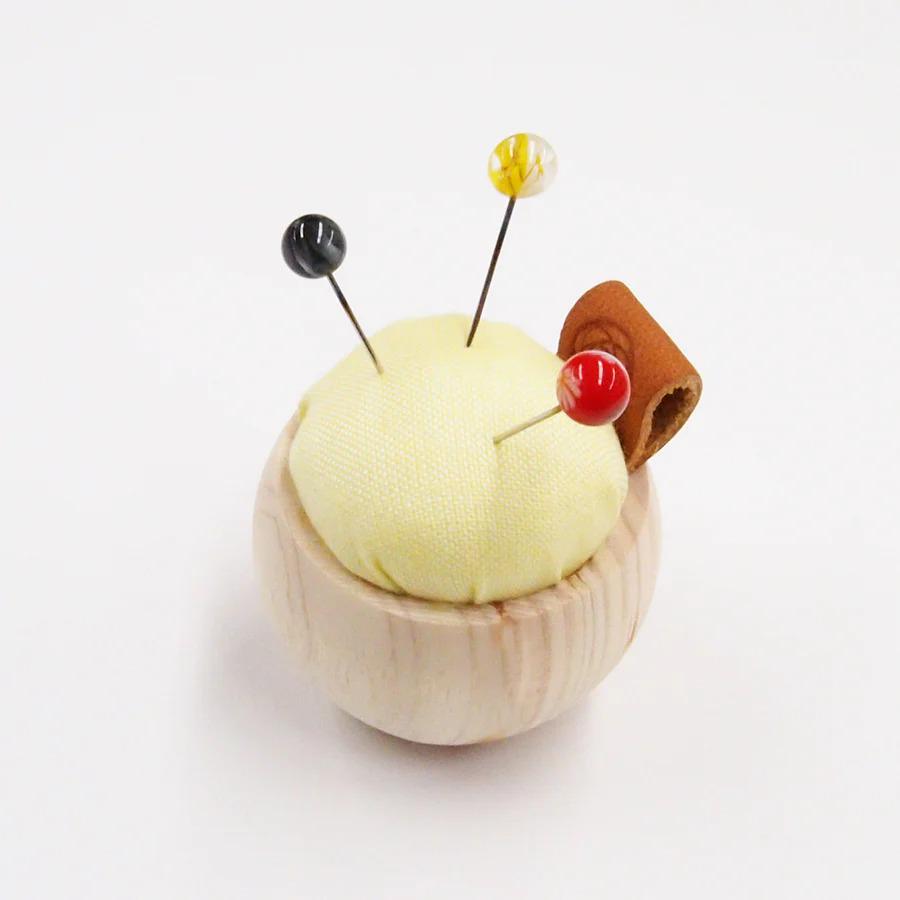 A wooden pin cushion with a yellow cushion, a red button, and a brown leather piece attached to it.