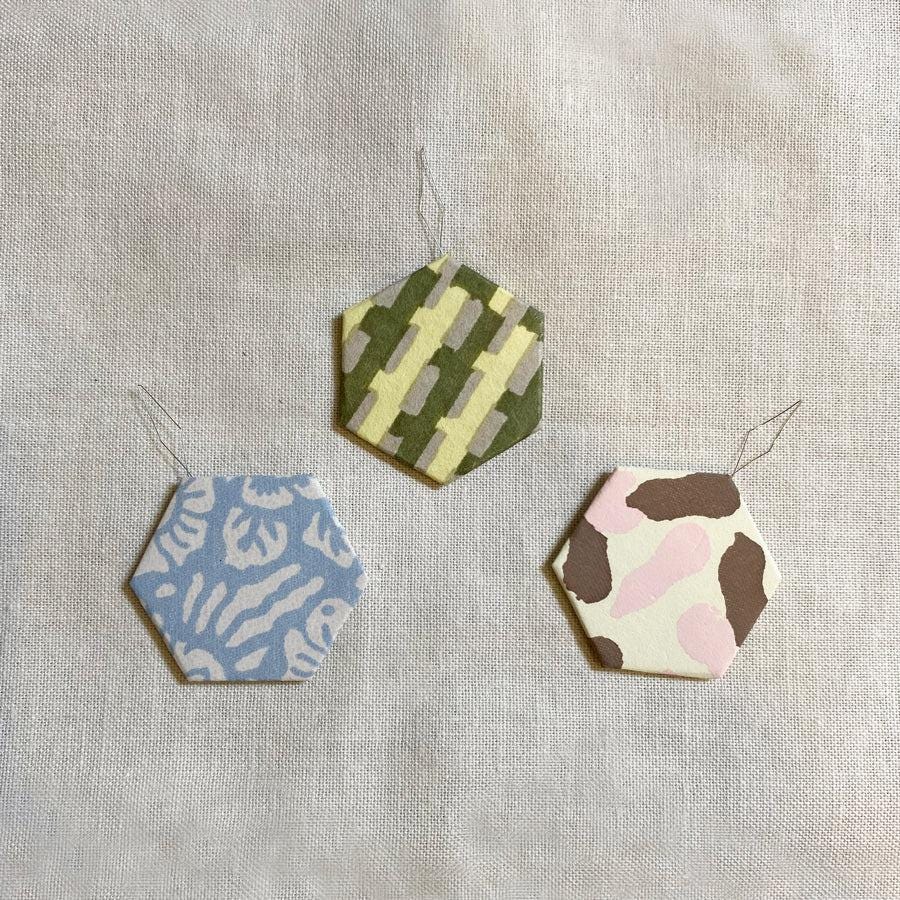 Three colorful hexagonal ornaments are displayed on a light-colored fabric background.