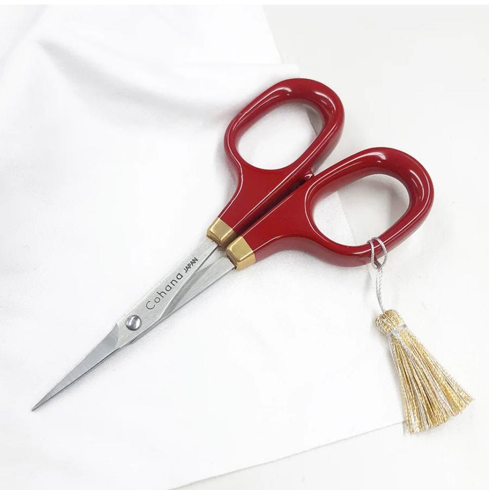 A pair of red scissors with gold accents and a gold tassel is resting on a white surface.