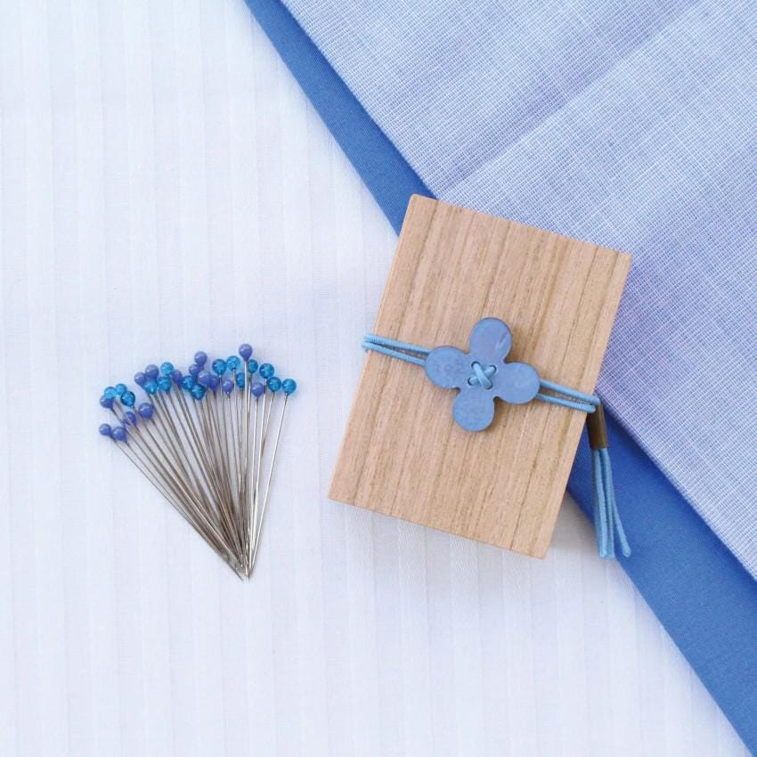 a collection of blue buttons and a wooden box with a blue flower-shaped button on it, all placed on a white surface with a blue and white striped pattern.