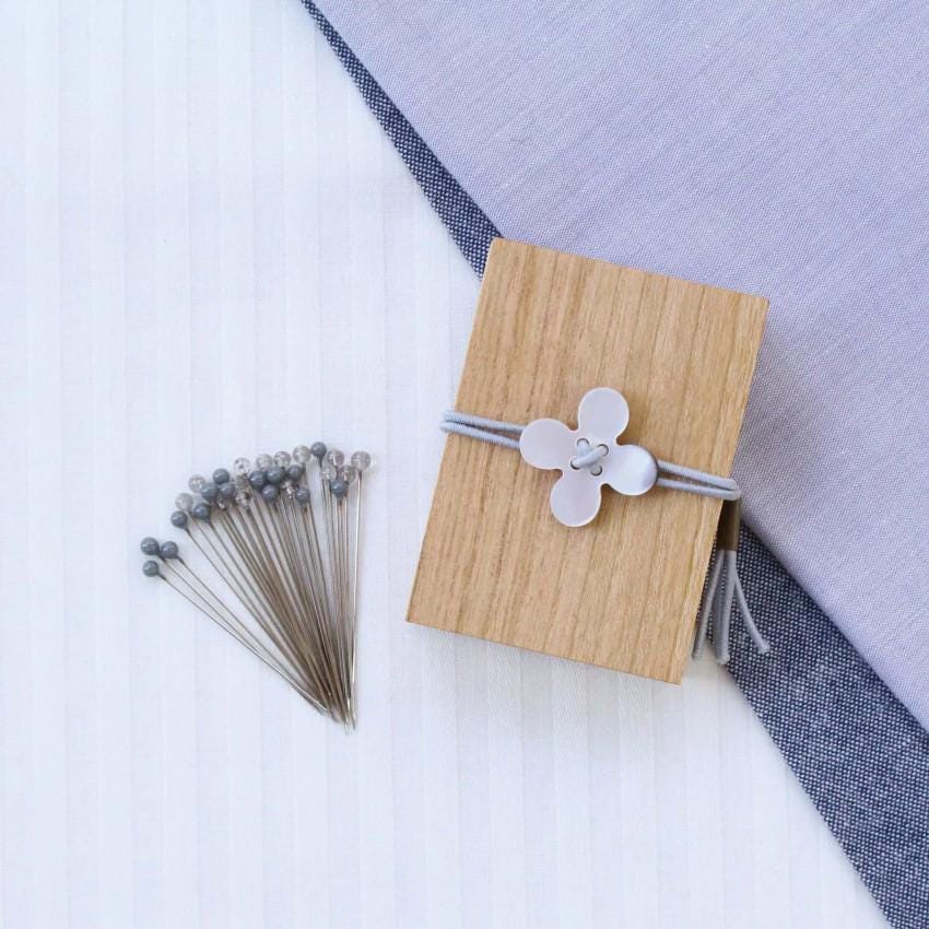 a wooden box with a white flower-shaped button on it, surrounded by several gray pins and a blue fabric.