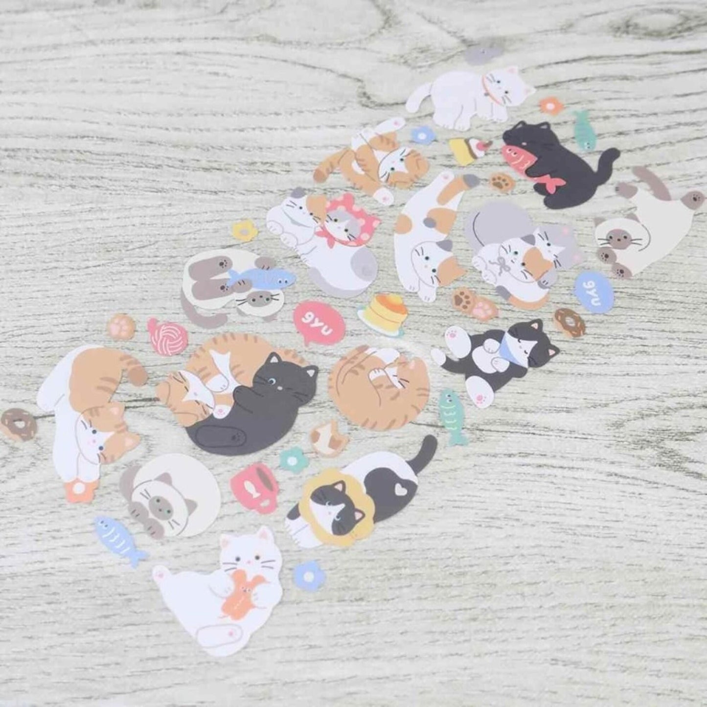 a collection of various cat-themed stickers and cutouts arranged on a wooden surface.