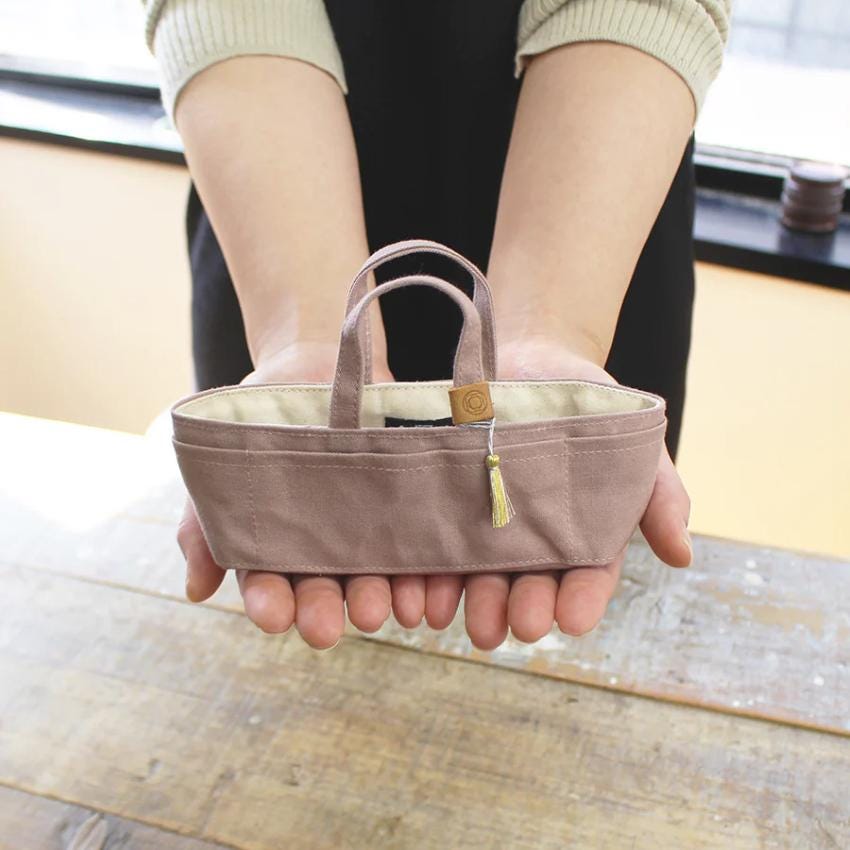 A person's hands holding a small, beige-colored purse or wallet.