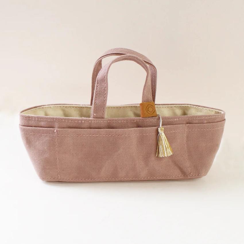 A pink tote bag with a tassel hanging from the handle, sitting on a white surface.