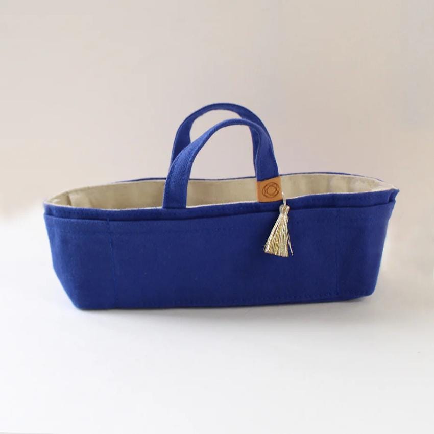 A blue tote bag with a tassel hanging from the handle, sitting on a white surface.