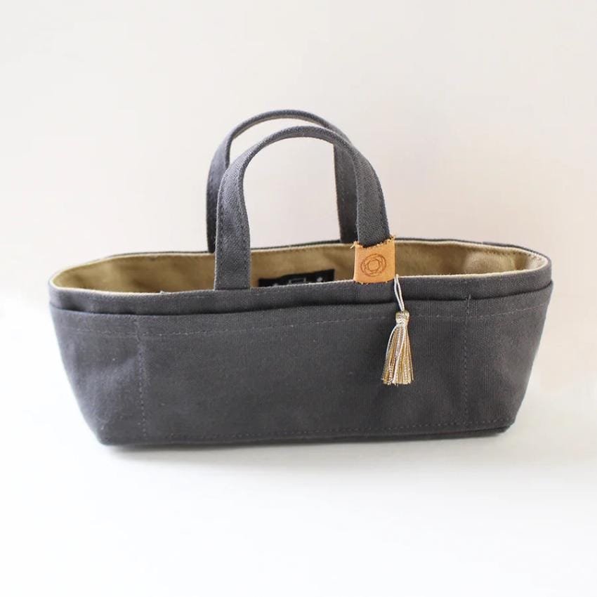 A gray tote bag with a tassel hanging from the handle, sitting on a white background.