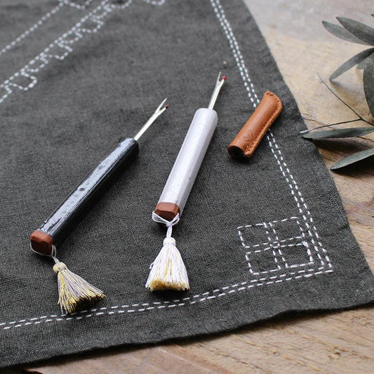 a collection of sewing tools, including a black and white tool, a white tool, and a brown tool, arranged on a gray cloth with a decorative border.