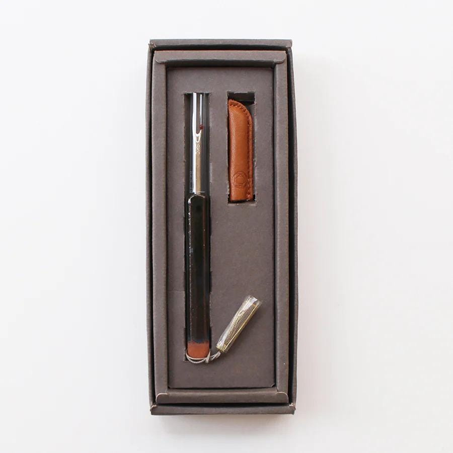 A black pen with a silver cap is placed inside a brown box, accompanied by a small leather case.