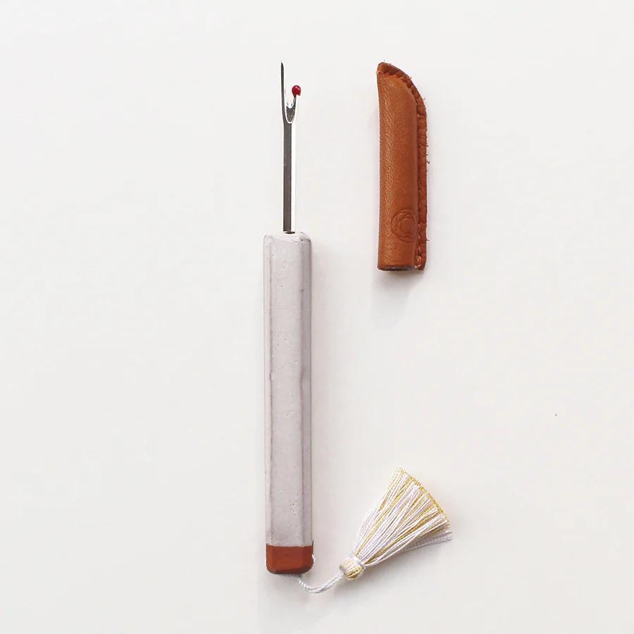 A white sewing needle with a red tip and a brown leather tassel are shown against a white background.