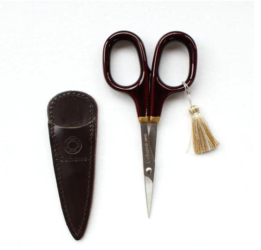 A pair of red-handled scissors with a tassel and a leather case with a logo are displayed against a white background.