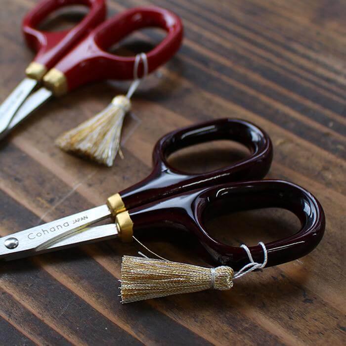 A pair of red and black scissors with gold tassels resting on a wooden surface.