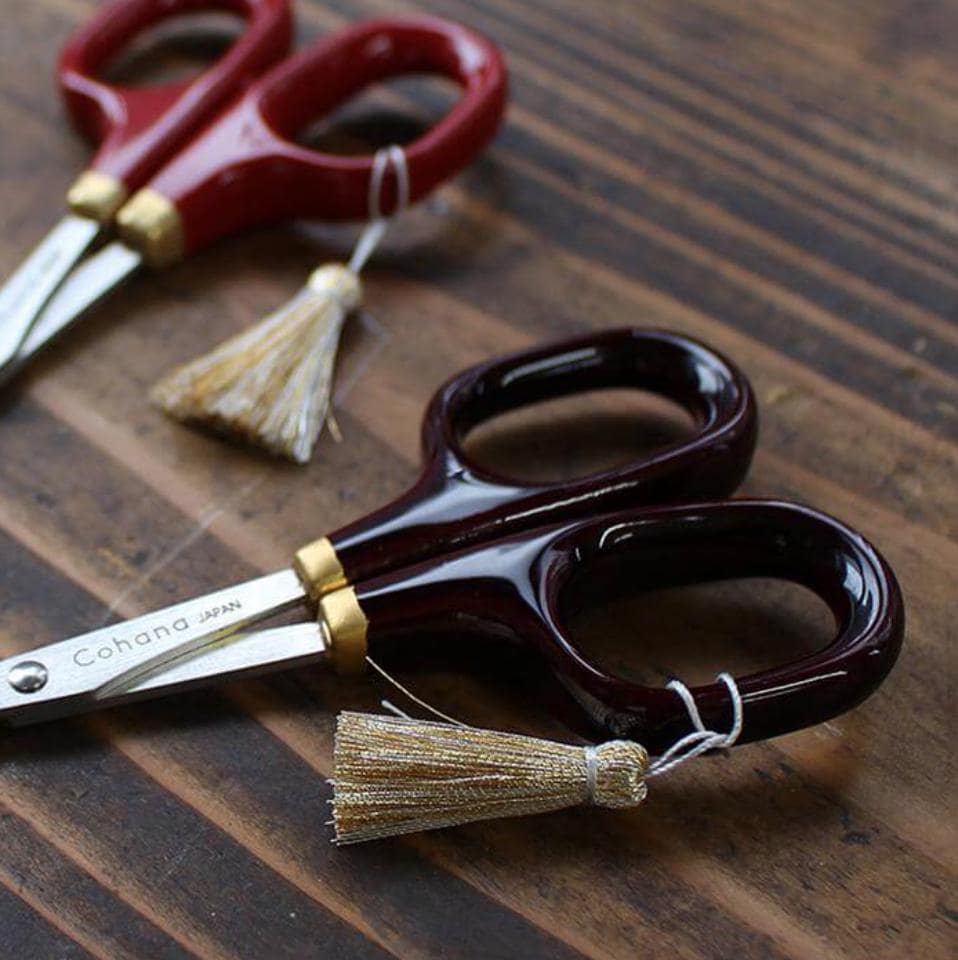 A pair of red and black scissors with gold tassels, resting on a wooden surface.