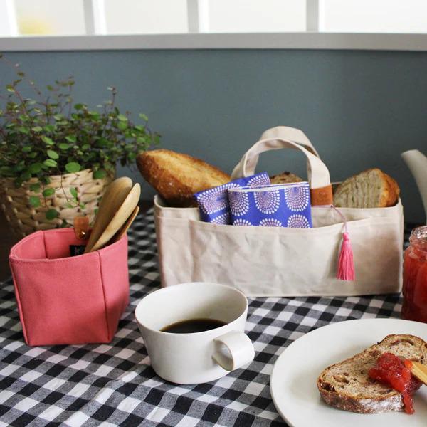 A cozy breakfast scene with a basket of bread, a cup of coffee, and a plate of toast, all set on a checkered tablecloth.