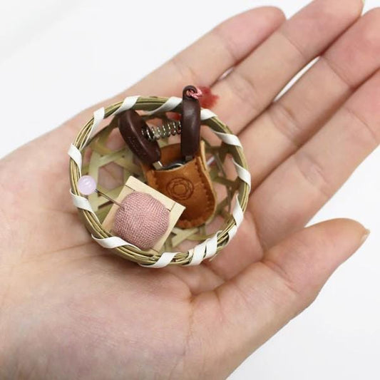 A hand holding a small woven basket containing various sewing and crafting tools, such as a needle, thread, and pins.