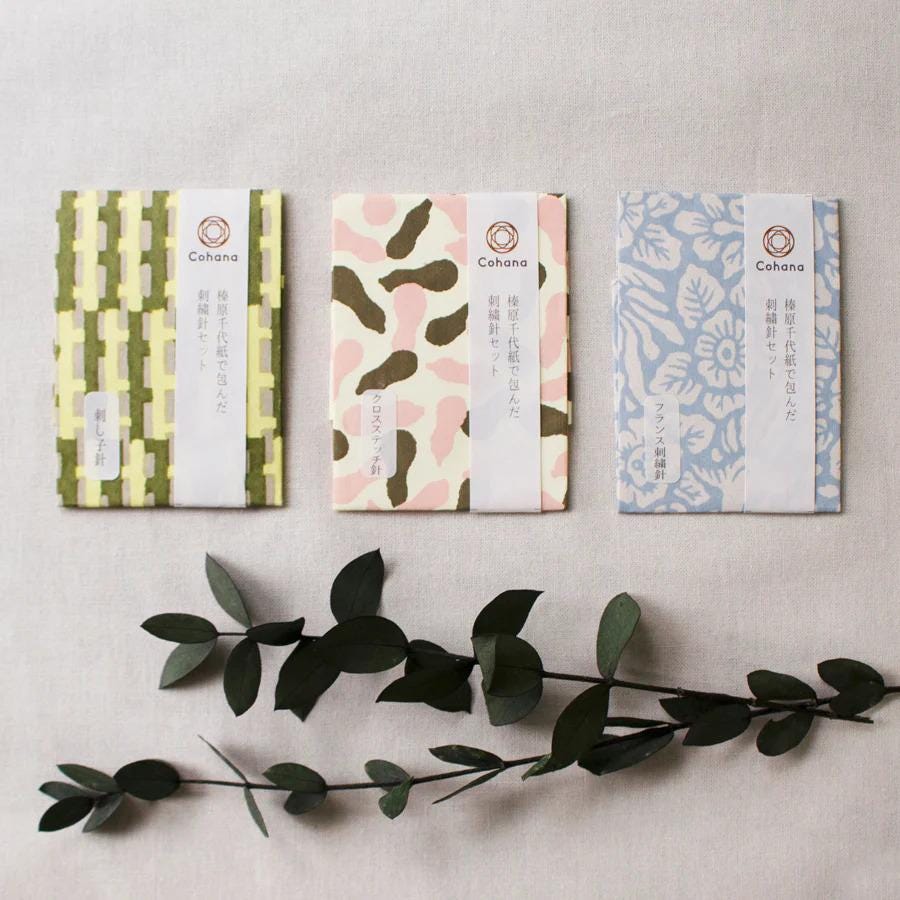 three different colored notebooks or pads with unique patterns, along with some green leaves and a branch.