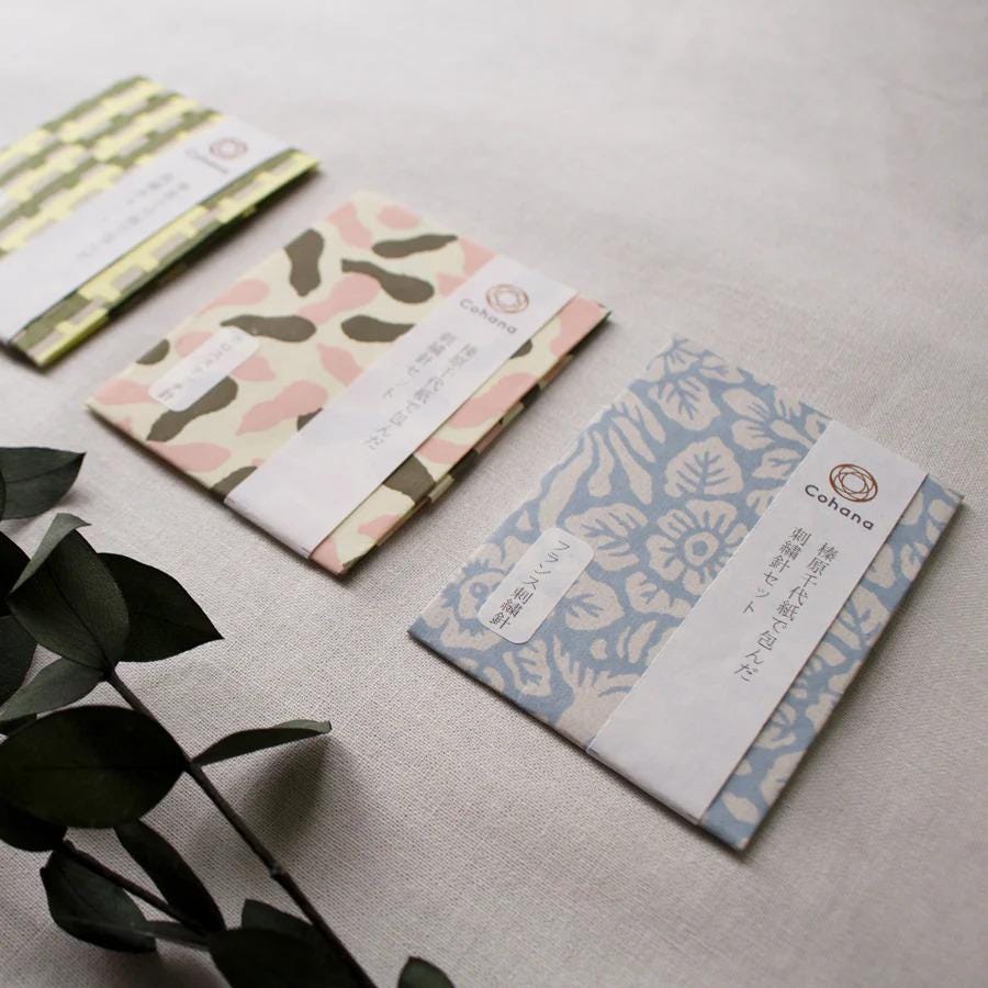 Three different colored paper bags or envelopes with Japanese text on them, placed on a light-colored surface.