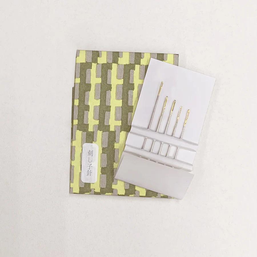 a set of sewing needles and a patterned paper with Japanese text on it, placed on a white surface.