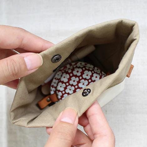 A person's hands holding a beige fabric pouch with a red and white floral pattern inside.