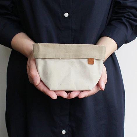A person is holding a small beige bag or pouch in their hands.