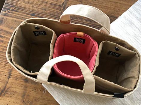 A beige tote bag with three compartments, each with a black label, is shown in the image.