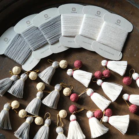 a collection of various tassel designs and spools of thread arranged on a wooden surface.