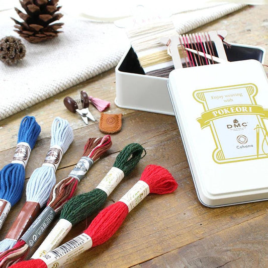 a collection of embroidery floss and needles on a wooden surface, along with a tin labeled "POKERI" and a sewing kit.