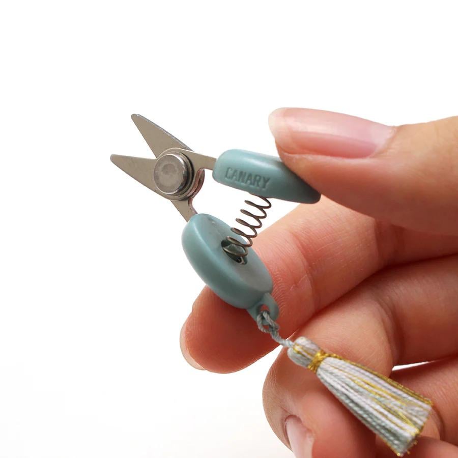 A hand holding a small pair of scissors with a tassel attached.