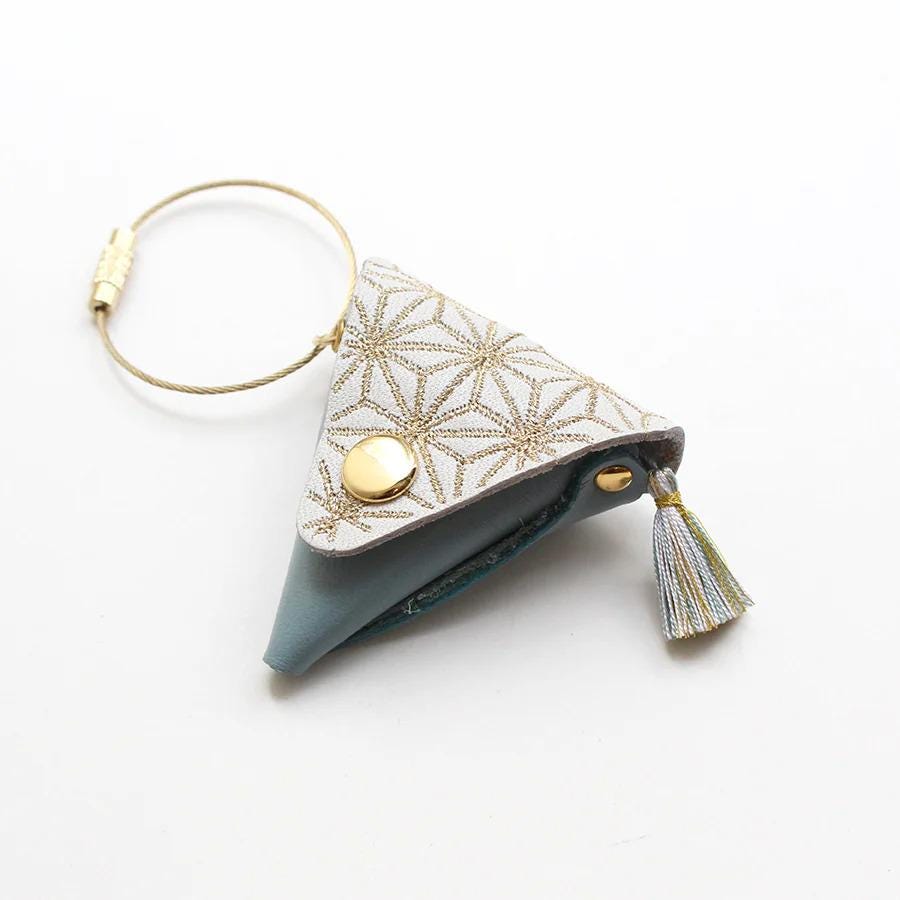A small, triangular-shaped keychain with a tassel hanging from the top.