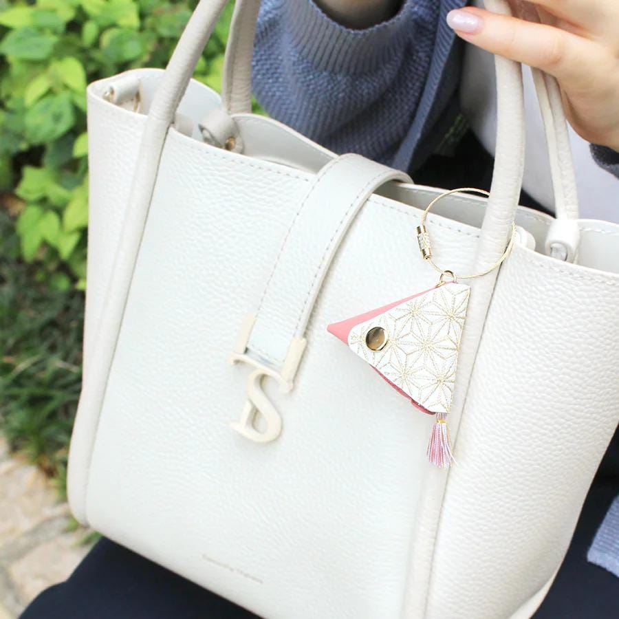A person is holding a white leather handbag with a floral keychain attached to it.